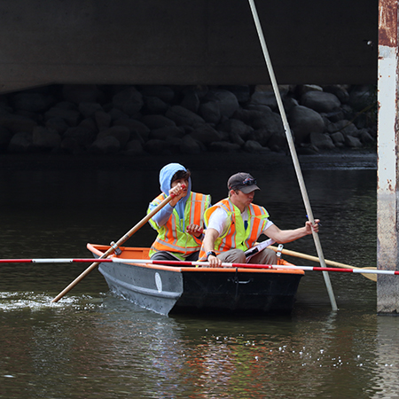Two interns in a canoe underneath a bridge.