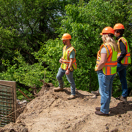 An engineer gives two interns a tour of a construction site.
