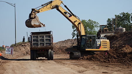 A yellow and black excavator drops dirt into the back of a truck.