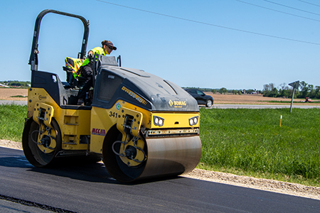 A woman operarating a asphalt roller on a rural road.
