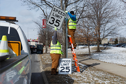 Two People switching out a speed limit sign.