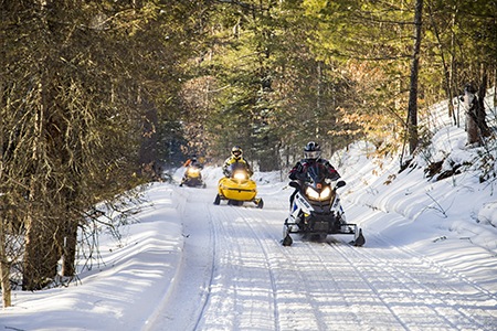 Three snowmobiles traveling on a snowmobile trail in the woods.