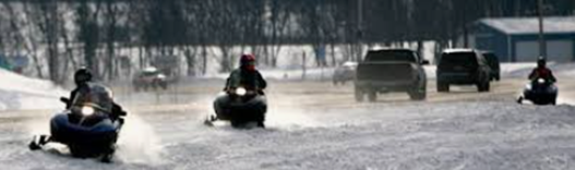 Snowmobilers traveling alongside a state highway with traffic.