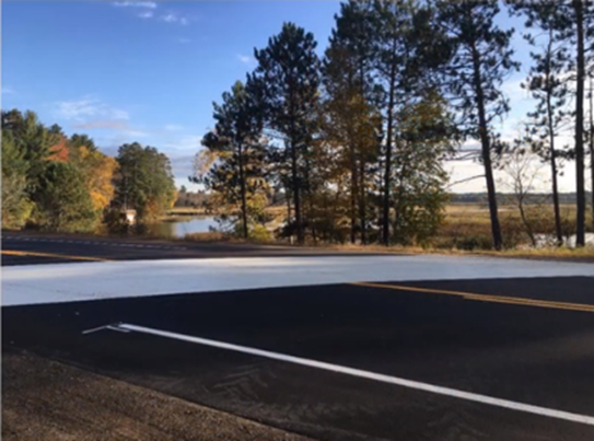 A white thermoplastic pavement coating covers a roadway.