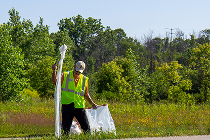 An Adopt-a-Highway volunteeer puts plastic waste into a garbage bag.
