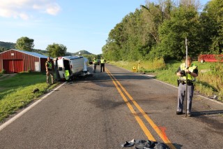 Officers standing outside a rolled over vehicle in the middle of a two-lane roadway in a rural area