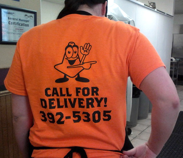 The back of an orange t-shirt, with a illustration of a construction cone and the words "Call For Delivery! 392-5305"