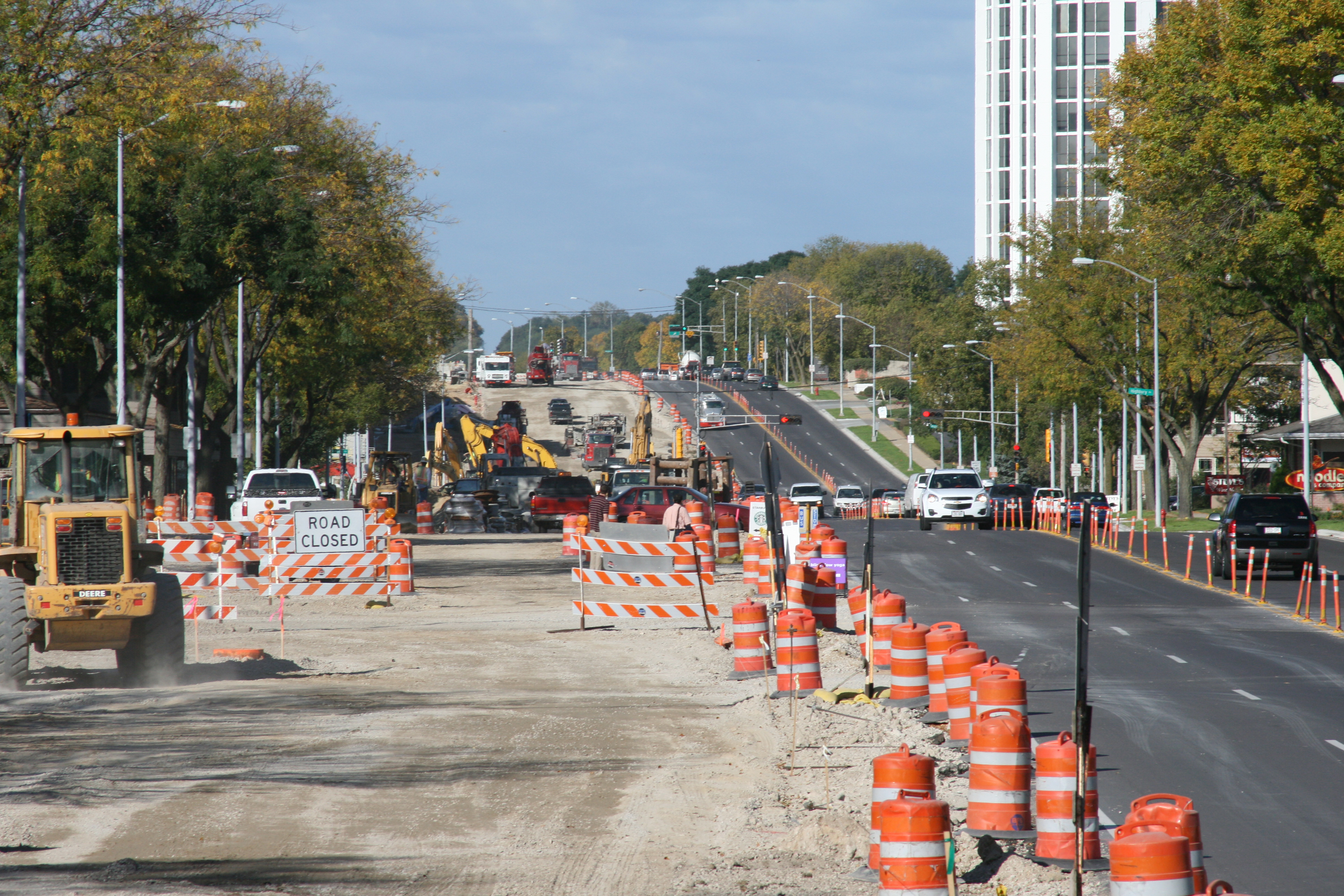 Orange construction barrels and a road closed sign are next to a road with three cars on it.