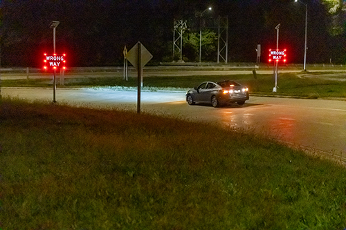 A car drives toward a flashing Wrong Way sign